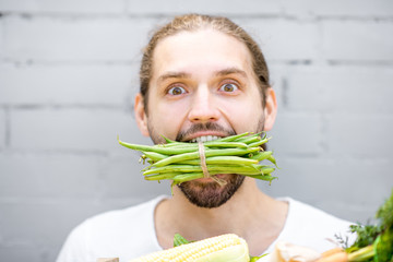 Close portrait of a handsome man biting green beans on the brick wall background