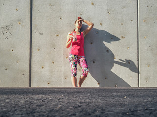  groggy sporty woman after fitness workout standing at a grey cement wall with shake bottle