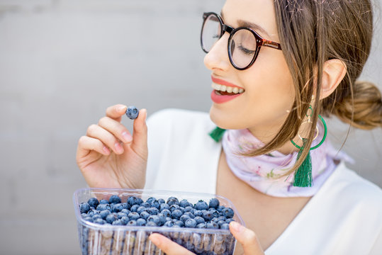 Young smiling woman eating bluberries outdoors on the gray wall background