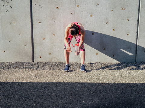  Groggy Sporty Woman After Fitness Workout Standing At A Grey Cement Wall With Shake Bottle