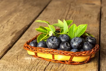 Foto op Plexiglas Wet blueberries in a small wicker basket. Freshly picked forest fruits on a wooden table. Sales of blueberries. Healthy summer refreshment. © martinfredy