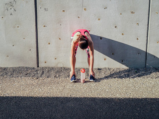 Fototapeta na wymiar groggy sporty woman after fitness workout standing at a grey cement wall with shake bottle