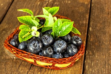 Wet blueberries in a small wicker basket. Freshly picked forest fruits on a wooden table. Sales of blueberries. Healthy summer refreshment.