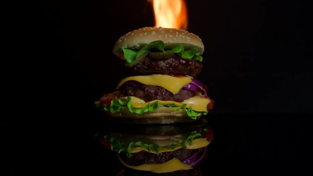 Delicious hot burger on the black mirror surface on fire. Black background for commercial