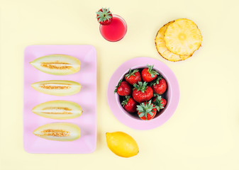 Fresh strawberries and melon on pastel yellow background.