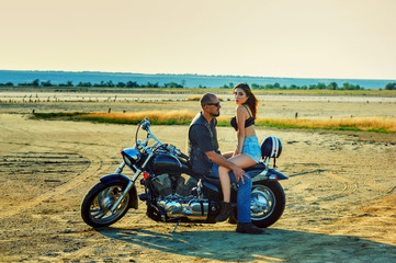 Young beautiful woman and man sitting on a motorcycle . A couple in love on a suburban Moto walk