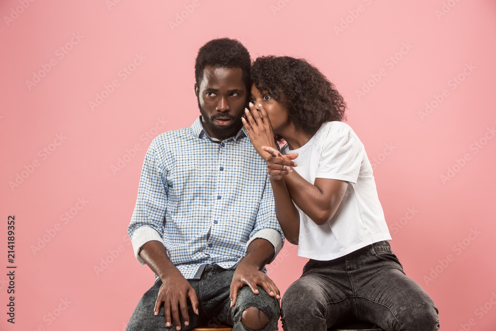 Wall mural The young woman whispering a secret behind her hand to afro man