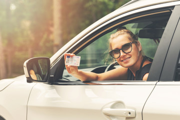smiling attractive woman showing her driver license out of car window