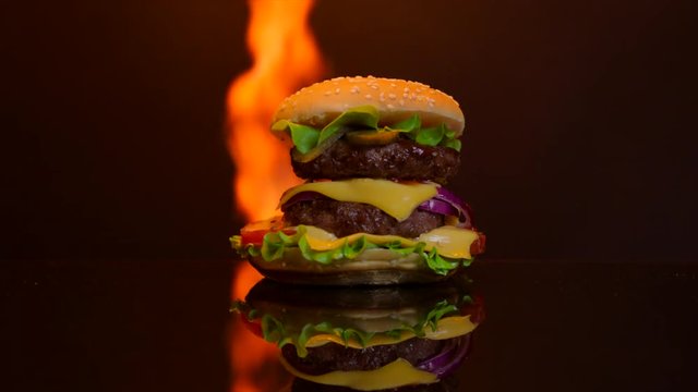 Delicious hot burger on the black mirror surface on fire. Black background for commercial