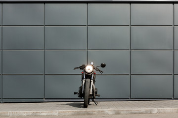 Craft motorcycle parking near gray wall of industrial building. Everything is ready for having fun driving the empty road on a motorcycle tour journey. Man hobby. Space for your individual text.