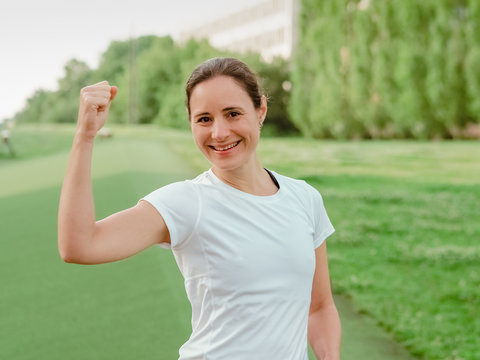 happy smiling femal Fitness Coach in white sportswear making fists outside in the park