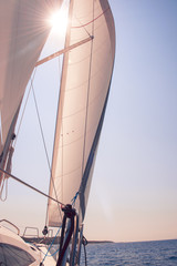 Sailboat with sun coming through between the sails among the islands of Croatia.