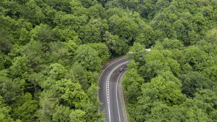 Aerial stock photo of car driving along the winding mountain pass road through the forest in Sochi, Russia. People traveling, road trip on curvy road through beautiful countryside scenery.