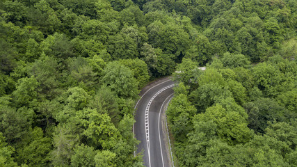 Fototapeta premium Aerial stock photo of car driving along the winding mountain pass road through the forest in Sochi, Russia. People traveling, road trip on curvy road through beautiful countryside scenery.