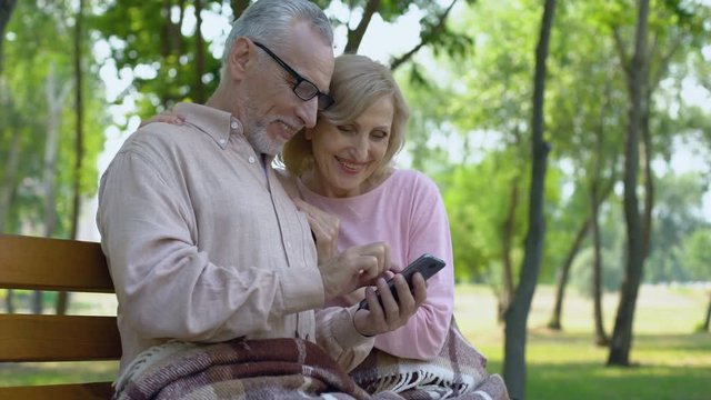 Grandfather and grandmother admiring children photos in smartphone application