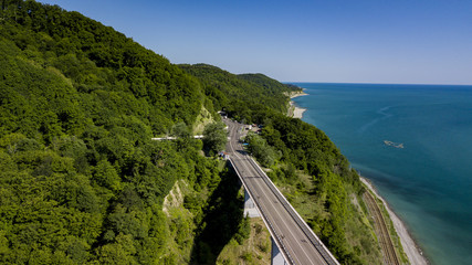 Aerial stock photo of car driving along the winding mountain pass road through the forest in Krasnodar Krai, Russia. People traveling, road trip on curvy road through beautiful countryside scenery.