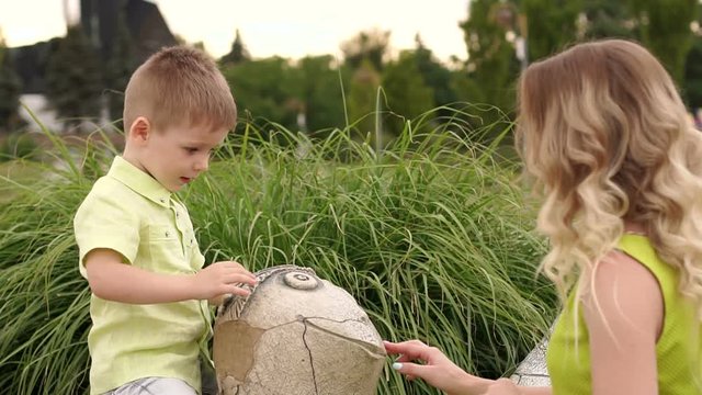 Mother and little son play in the Park in warm summer weather with a stone statue of a turtle.