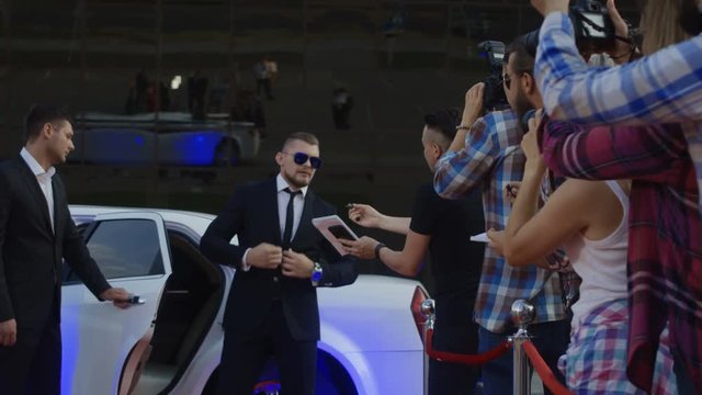 Cool famous actor walking out of limo and posing for photographers while giving autographs on red carpet