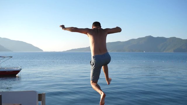 happy male jumps from jetty in summer sea on background of mountains and sky on weekend