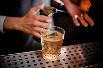 Barman making a fresh summer old fashioned cocktail with orange peel and smoke note