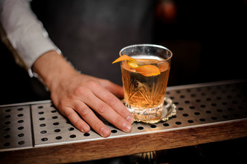 Barman hand with a glass of fresh old fashioned cocktail with orange peel