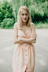 Blondie woman in pink dress in summer forest. Young stylish pretty girl dancing and have fan outdoor, have a good time in park on vacations. Natural, beauty, happiness concept