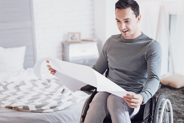 Working at home. Handsome differently abled male sitting on his wheelchair and keeping smile on face