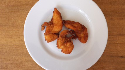 Pieces of meat appetizing chicken in breaded. The chicken on the plate rotates against the background of the wooden table. Top view, close-up.