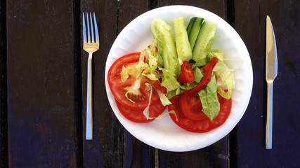 Close-up shot. A salad of fresh vegetables rotates on a white plate. Wooden table. Salad of tomatoes and cucumbers is spinning.