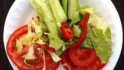 Close-up shot. A salad of fresh vegetables rotates on a white plate. Wooden table. Salad of tomatoes and cucumbers is spinning.