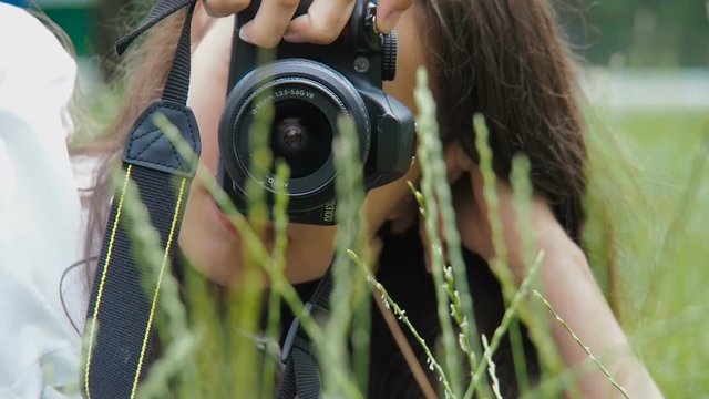 A girl photographer is working in nature. The girl with the camera lies in the grass.