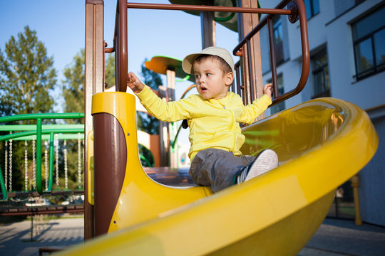 Nice cute boy of three years in a yellow jacket is playing on a bright playground.