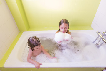 Happy laughing sister kids taking a bath playing with foam bubbles. Little children in a bathtub. Family lifestyle indoors
