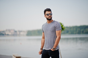 Fototapeta na wymiar Handsome tall arabian beard man model at stripped shirt posed outdoor. Fashionable arab guy at sunglasses.