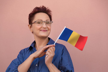 Romania flag. Woman holding Romanian flag. Nice portrait of middle aged lady 40 50 years old with a national flag over pink wall background outdoors - 214200394