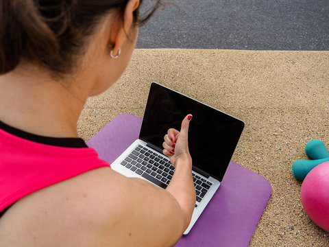 female fitness coach making  thumbs up infront of a laptop on a mat after an successful online workout