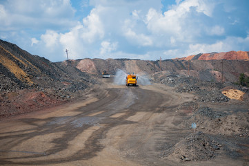 Heavy truck pours the road with water in the iron ore quarry. Dust removal, protection of the environment. Irrigation of the road from dust © Yevhen