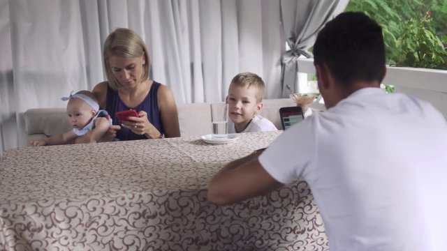 Little boy has fun with parents using phones in cafe