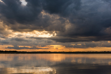 Sunset in the lake. Beautiful sunset behind the storm clouds before a thunder storm above the over lake landscape background. Dramatic sky with cloud at sunset.