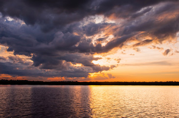 Fototapeta na wymiar Sunset in the lake. Beautiful sunset behind the storm clouds before a thunder storm above the over lake landscape background. Dramatic sky with cloud at sunset.