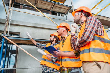 group of builders in hard hats and reflective vests pointing at building house