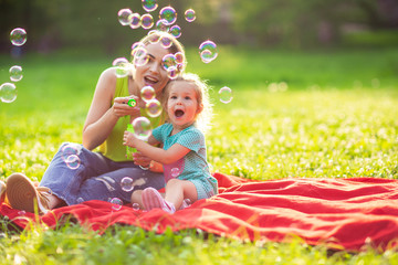 Family in park -Female child blows soup foam and make bubbles with her mother in nature