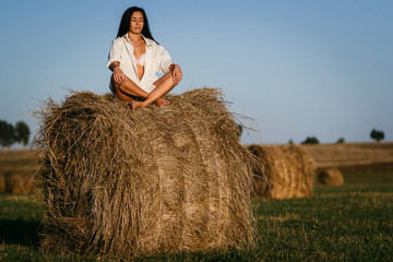 Naklejka na ściany i meble beautiful tanned brunette girl sitting in Lotus position on a haystack