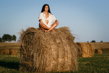 Naklejka na ściany i meble beautiful tanned brunette girl sitting in Lotus position on a haystack