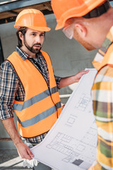 builders with blueprint having conversation at construction site