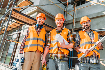 bottom view of group of happy equipped builders looking at camera at construction site