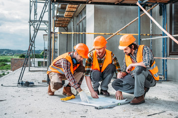 close-up shot of group of happy builders having conversation about building plan