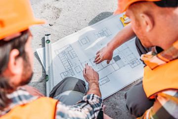 high angle view of builders pointing at blueprint