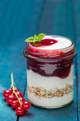 Rote Grütze mit Joghurt und Haferflocken in einem Einmachglas auf Holzuntergrund