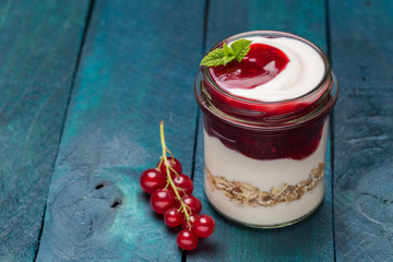 Rote Grütze mit Joghurt und Haferflocken in einem Einmachglas auf Holzuntergrund
